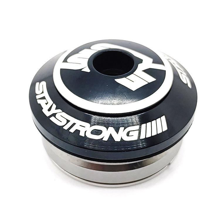 A metallic cylindrical object with the label "STAYSTRONG" in white letters, featuring a circular design at the top surrounded by additional white markings. Designed for a 1.1/8" Integrated Frame, this Stay Strong Integrated Icon Headset includes sealed bearings for superior performance and durability.