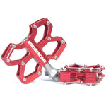 Red aluminum Stay Strong Axis Junior Platform Pedals with "STAYSTRONG" branding, featuring multiple pins for grip, sealed bearings, and a central metal spindle. The pedals, made from alloy extrusion CNC, are displayed against a plain white background.