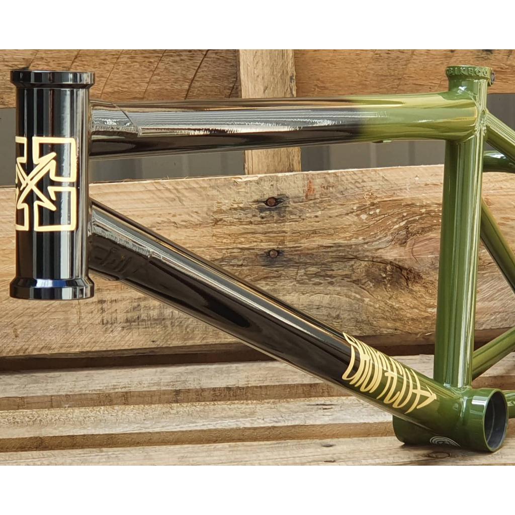 Close-up of the Fit Bike Co Shortcut Frame, showcasing green and black paint with gold decals, resting on a wooden pallet.