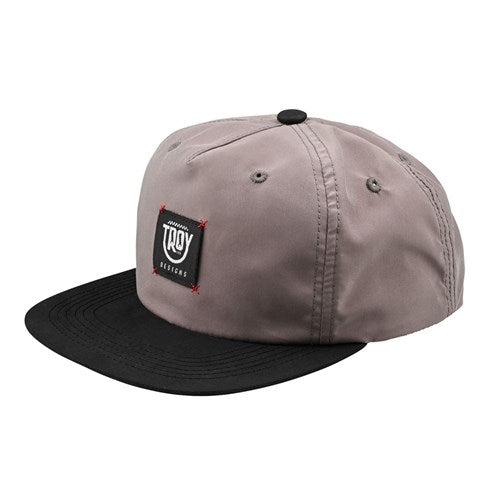 Gray TLD 25.1 Smiley Unstructured Snapback with a black brim, featuring a playful "Troy Lee Designs" logo patch on the front for a fun and casual look.