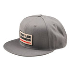 A grey baseball cap with a flat brim features a front patch displaying "Troy Lee Designs," embodying the TLD 25.1 Factory Hat's top-tier style.