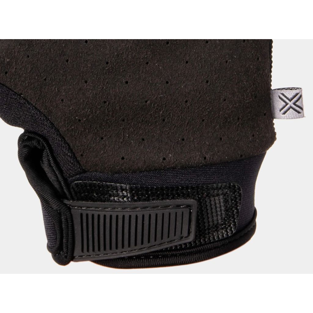 Close-up of a black Fuse Alpha Youth Glove with a textured surface, featuring silicone grips and a Velcro strap. The reinforced thumb area enhances durability, while an "X" logo tag adorns the side.