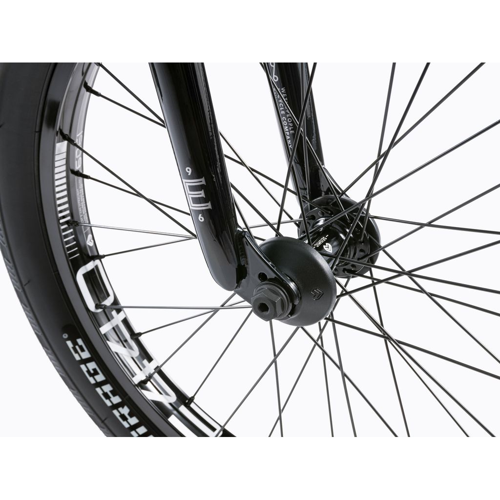 Close-up of a Wethepeople Envy 20 Inch BMX Bike's front wheel, featuring black spokes, hub, and tire section. The fork has markings with tire brand text, showcasing the robust Chromoly frame of this BMX bike.