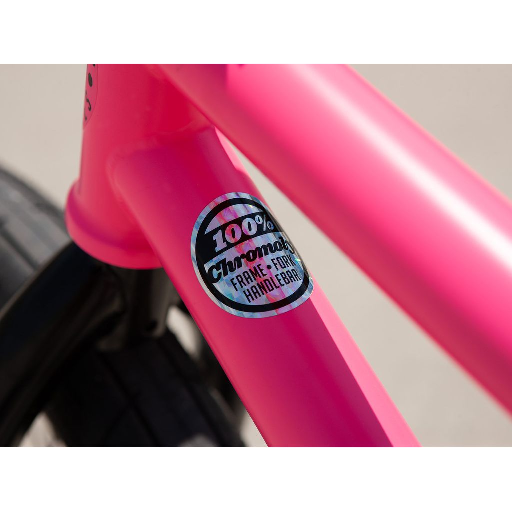 Close-up of a vibrant pink frame from the Sunday Street Sweeper 20 Inch Bike, featuring a sticker that reads "100% Chromoly Frame, Fork, Handlebar," positioned next to a black tire.