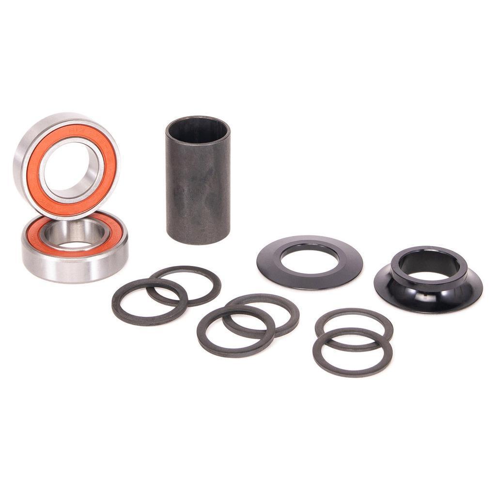 The Salt Rookie Mid Bottom Bracket, including ball bearings, rings, a cylindrical spacer, and two black circular components, is arranged on a white surface to provide smooth performance for 19mm spindle cranks.