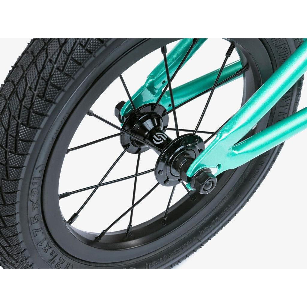 Close-up of a teal Wethepeople Prime Balance BMX Bike wheel featuring black spokes and a knobby tire, available for pre-order.