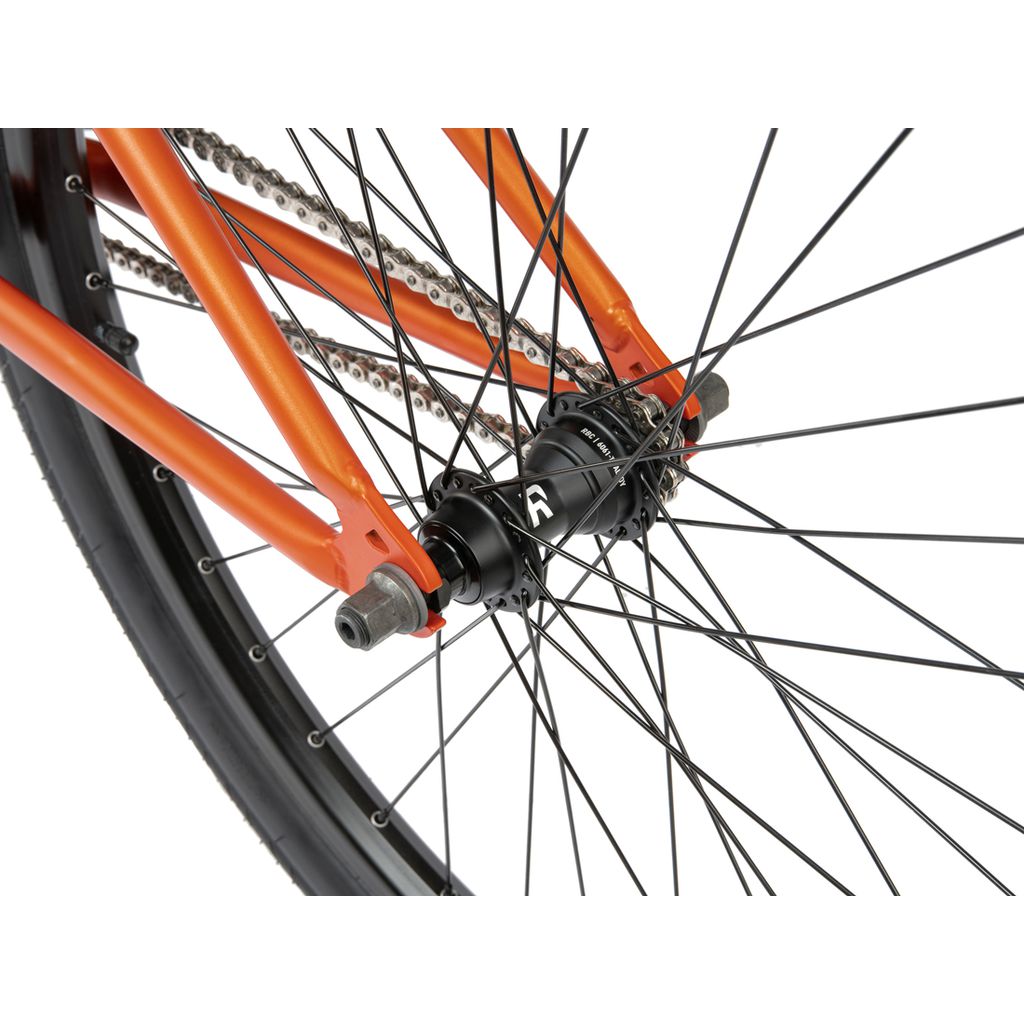 Close-up view of the rear wheel of a Radio 26 Inch Ceptor Bike with an orange frame, showing the spokes, hub, sealed bearings, chain, and part of the tire.