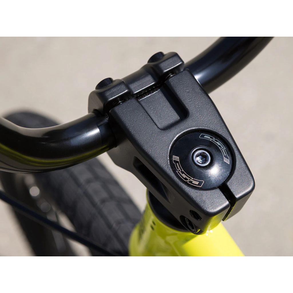 Close-up of the handlebar and stem on a Sunday Primer 18 Inch Bike (2025). The black stem is affixed to a yellow BMX frame and features a black bolt cap adorned with metallic accents, highlighting its Pro-Style geometry.