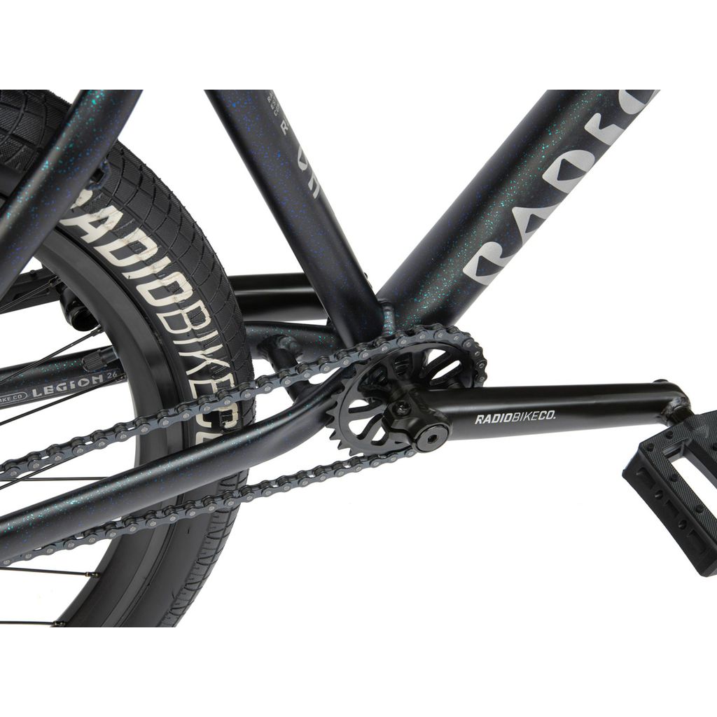 Close-up view of a black RADIOBIKECO. bicycle's pedal, crank arm, chain, and rear tire with "Radio 26 Inch Legion Bike" visible on the frame and tire. The sturdy 6061-T6 alloy frame ensures durability and performance on every ride.