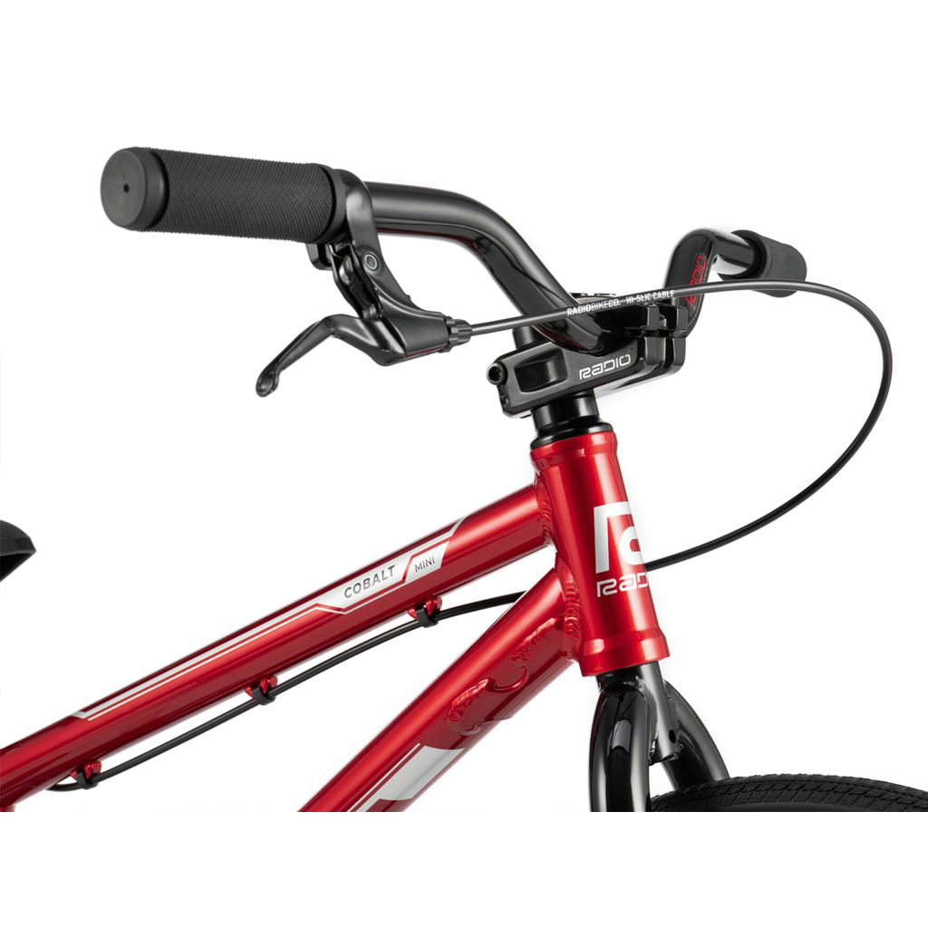 Close-up of a red bicycle's handlebar and front frame area, featuring brake levers, ergonomic grips, and the word "Radio Cobalt Mini Bike" on the frame from the Cobalt range.