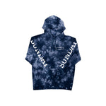 A navy and white tie-dye hooded sweatshirt with the word "SUNDAY" printed in white along both sleeves and a small logo on the chest, called the Sunday Rockwell Box Hoodie.