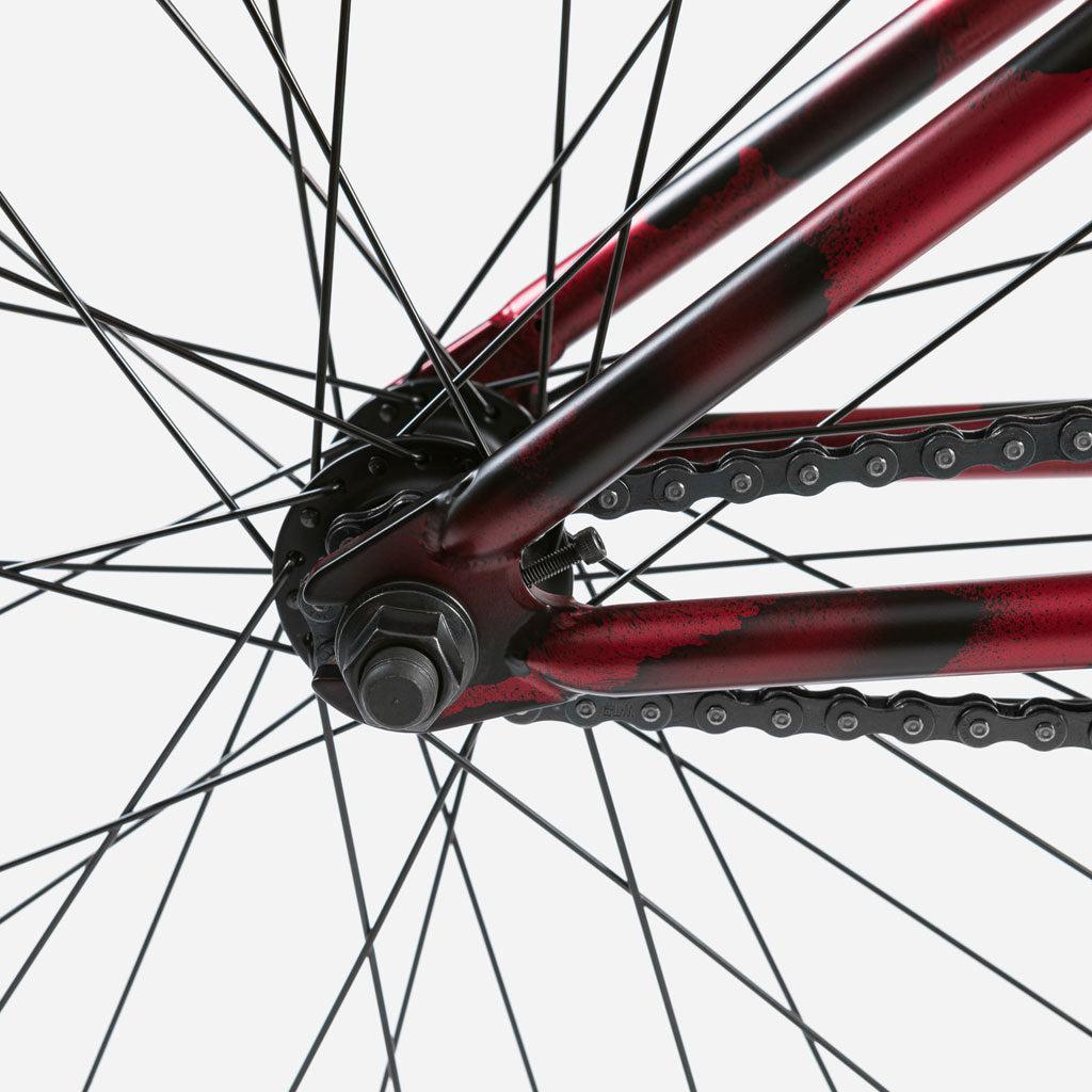 Close-up of the Wethepeople Audio 22 Inch Bike's rear wheel and chain, highlighting the red spokes, hub, and chain tensioner against a plain white background.