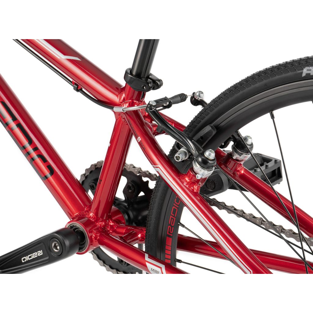 Close-up of a red bicycle's rear frame, showcasing the brake mechanism, chain, and part of the wheel with tire—perfect for BMX racing enthusiasts seeking durable components from the Radio Cobalt Mini Bike.