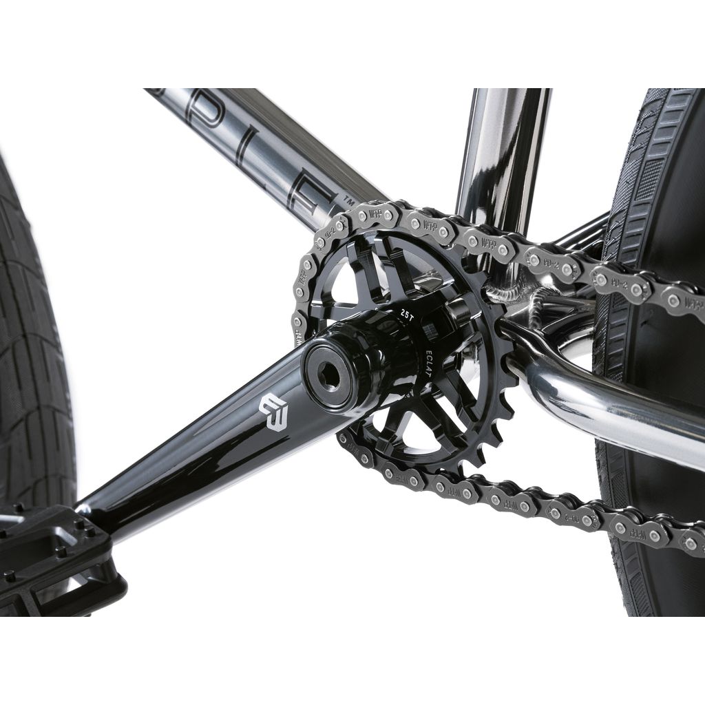 Close-up of a Wethepeople Envy 20 Inch BMX Bike's black metallic crankset, chainring, and rear wheel. The chain rests on the cog against the durable chromoly frame, which is partially visible.