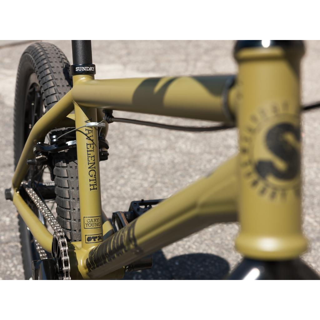 Close-up of a Sunday Wave Length 20 Inch (Gary Young) bike with a yellow frame, black tires, and visible chain featuring Odyssey parts, parked on concrete.