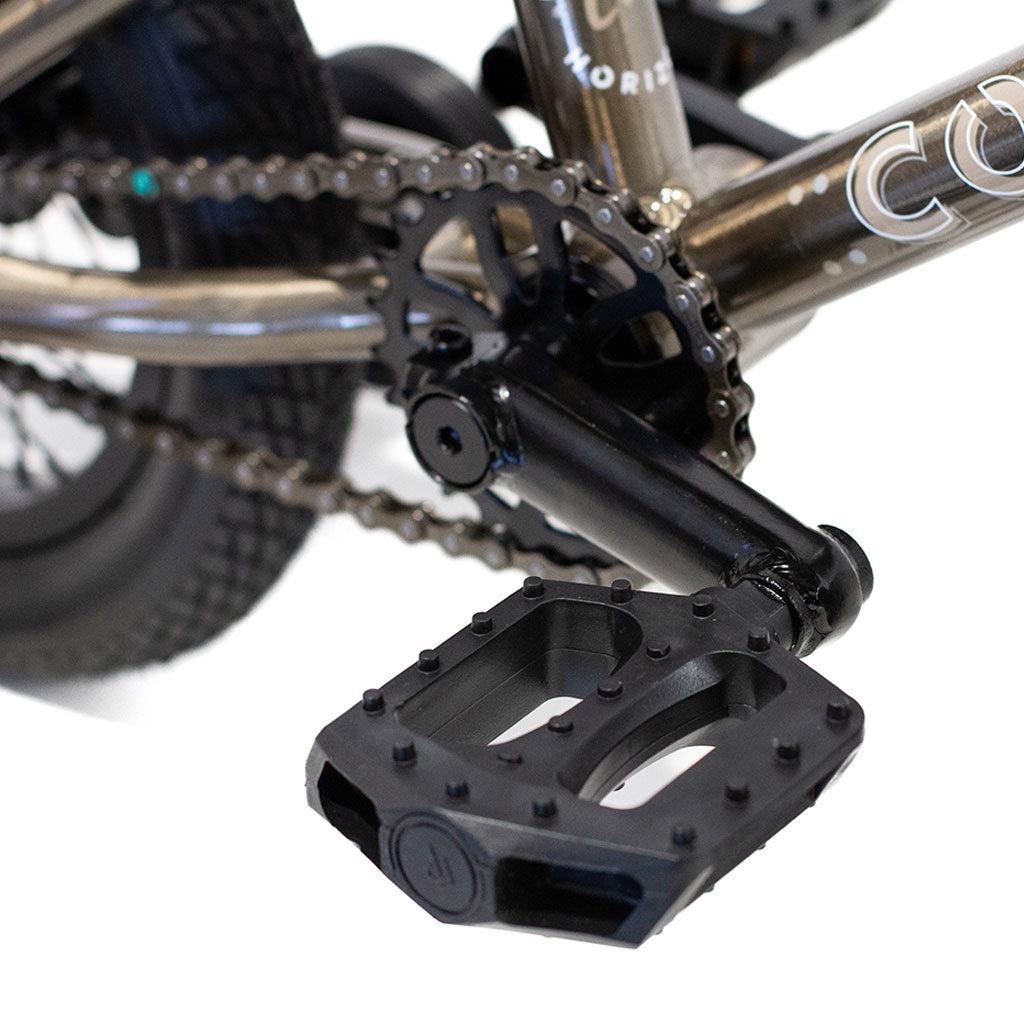 Close-up of a Colony Horizon 12 Inch Bike's black metal pedal attached to the crank arm, with the chain and rear wheel visible in the background.