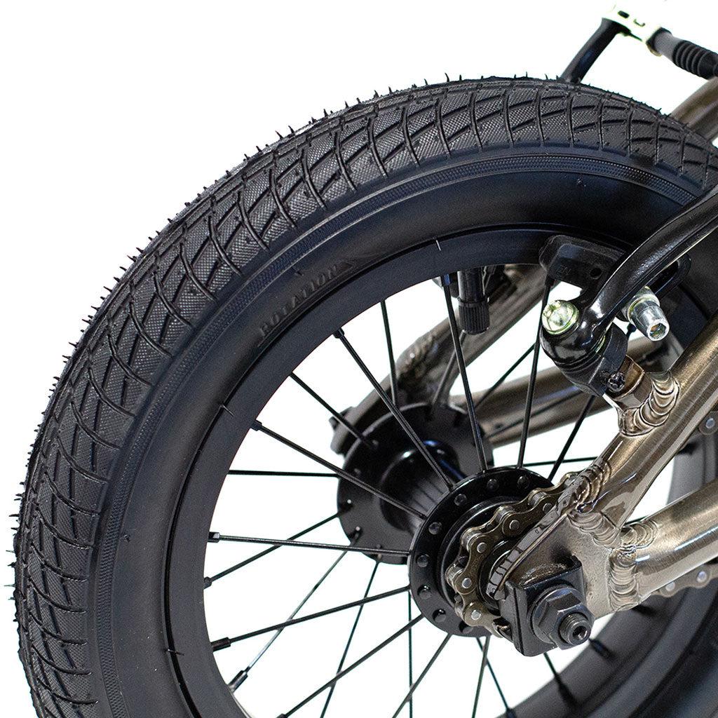 Close-up of the rear wheel of a Colony Horizon 12 Inch Bike, showcasing its thick, knobby tire, disc brakes, spokes, hub, part of the chain, and its lightweight alloy frame.