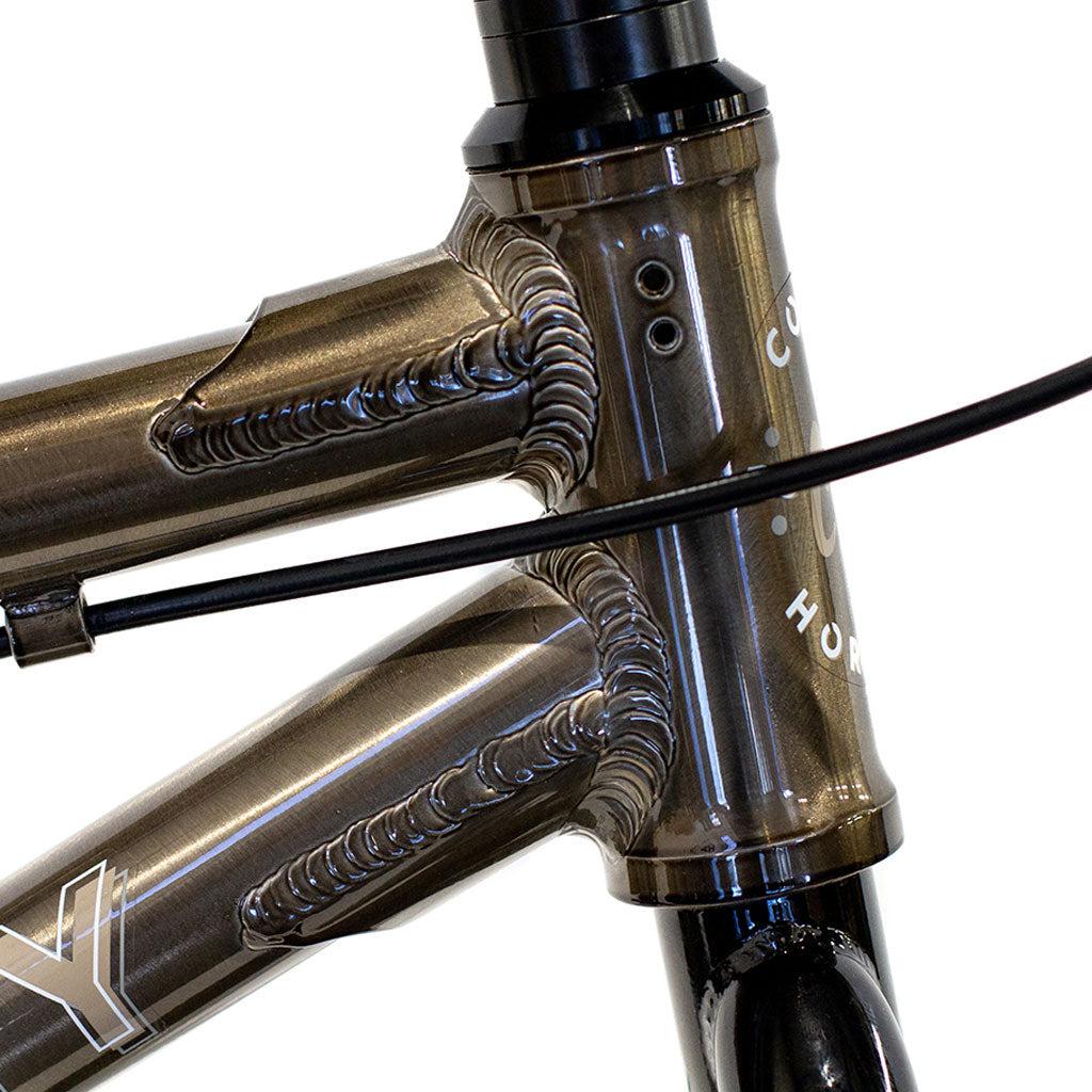 Close-up of the bronze-colored frame of the Colony Horizon 14 Inch Bike, highlighting the intricate welds, a black cable, and partially visible brand markings on the head tube.