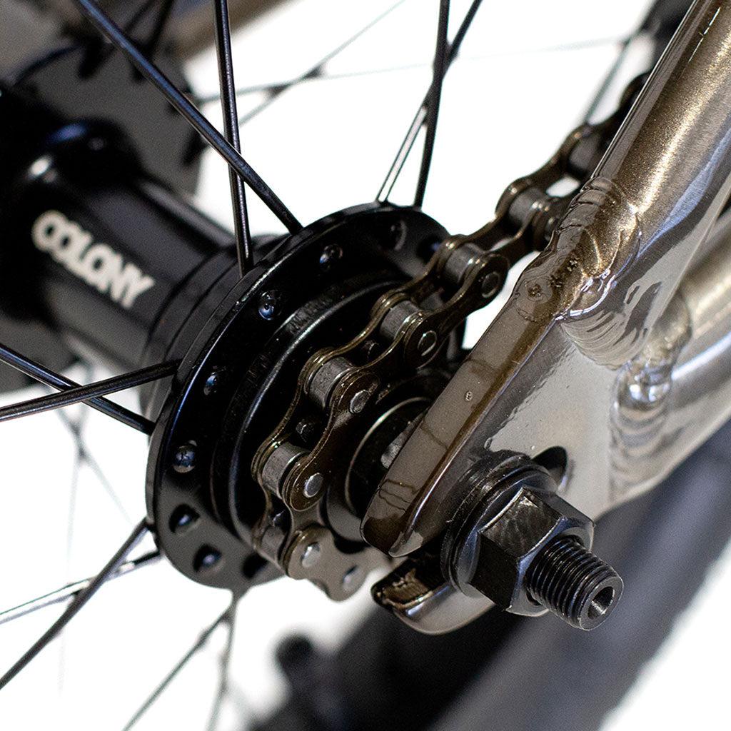 Close-up of the rear wheel hub on the Colony Horizon 14 Inch Bike, showcasing the chain and axle components under a spotlight. The Colony brand is prominently displayed on the hub, emphasizing its precision engineering.