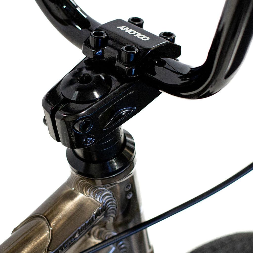 Close-up of the Colony Horizon 14 Inch Bike's handlebar stem and head tube, highlighting a black handlebar clamp branded "COLONY." The metallic frame with visible welds exemplifies its lightweight alloy construction.