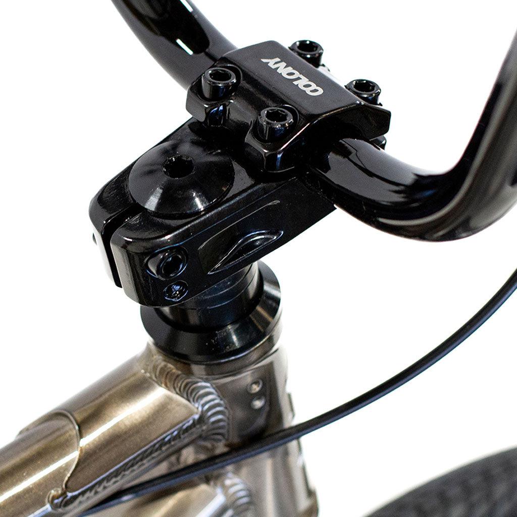 Close-up view of the Colony Horizon 20 Inch Freestyle Bike's handlebars and stem, showcasing a glossy black finish against a sleek metallic frame. The handlebar clamp is prominently displayed with bolts, making it ideal for any freestyle Olympic athlete.