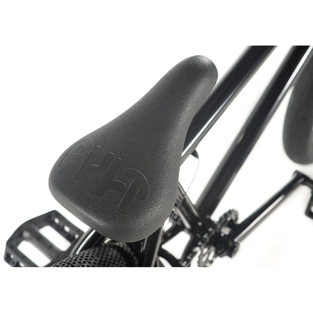 Close-up of a Cult Gateway 20 Inch Bike seat with embossed text, black pedals, and part of the frame visible, highlighting modern geometry for premium quality.