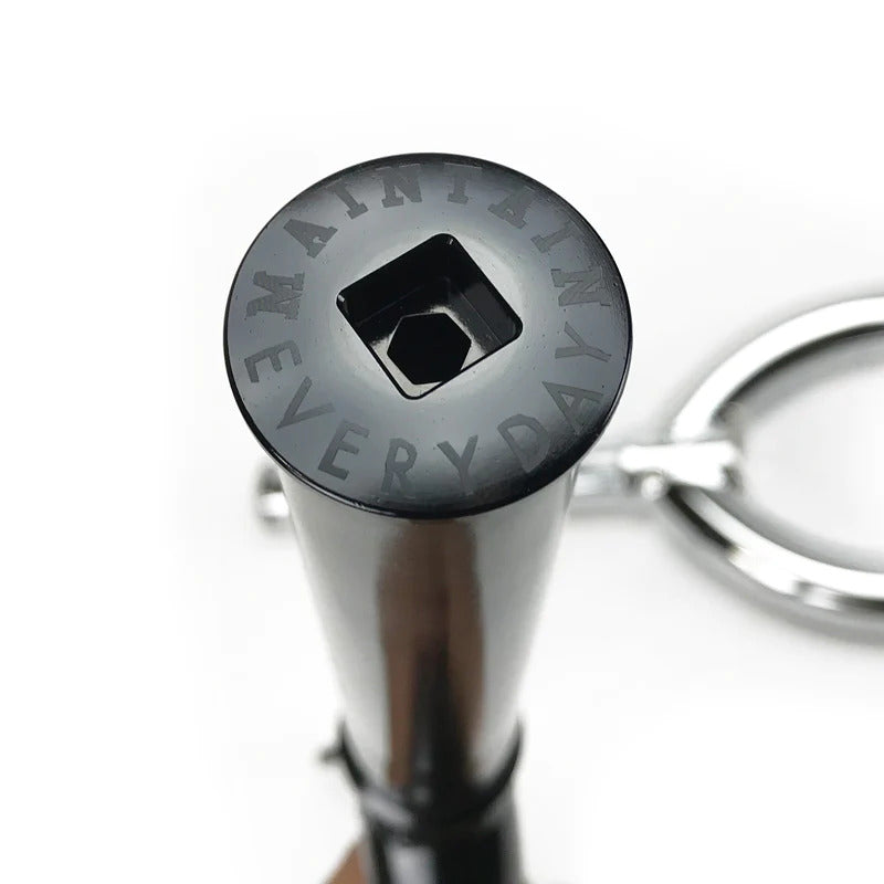 Close-up of a keychain tool in black, ideal for BMX enthusiasts, featuring "MAINTAIN EVERYDAY" engraved around the hexagonal hole, reminiscent of the Cult Sect V4 20 Inch Forks. It comes with a metal key ring attached.