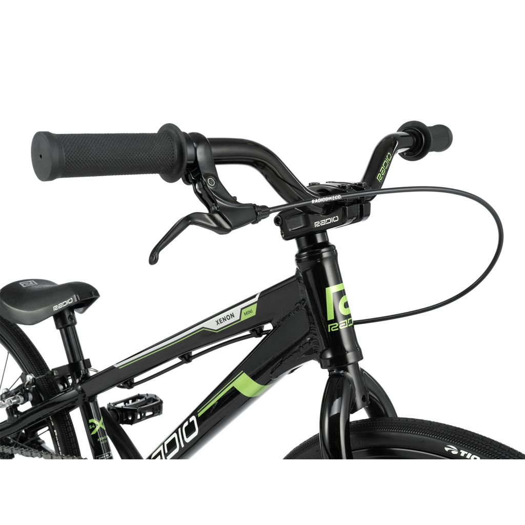Close-up of the handlebars and front part of a black Radio Xenon Mini Bike with green accents and the brand name "Radio" on the frame. The image shows the brake lever, grips, hydro-formed 6061-T6 alloy frame, and part of the front wheel, capturing the premium design of this BMX race bike.