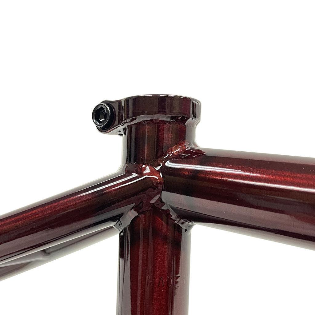 Close-up of a glossy red bicycle frame joint, featuring the S&M C.C.R. (Clint Reynolds) 14mm Dropout Frame, seamlessly connecting the top tube and seat tube with a mounting point.