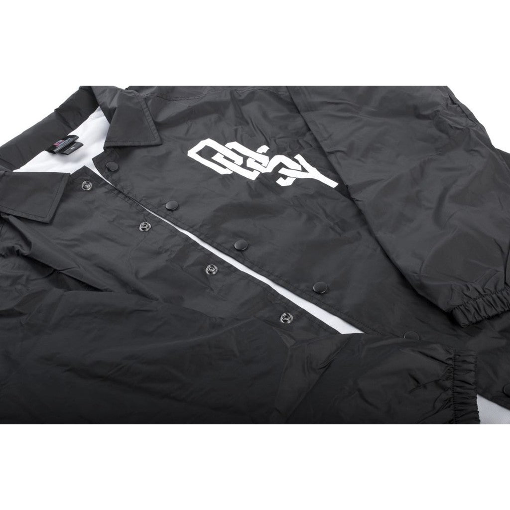 A black Odyssey Varsity Coach Jacket with elastic cuffs and a white stylized graphic on the left chest.