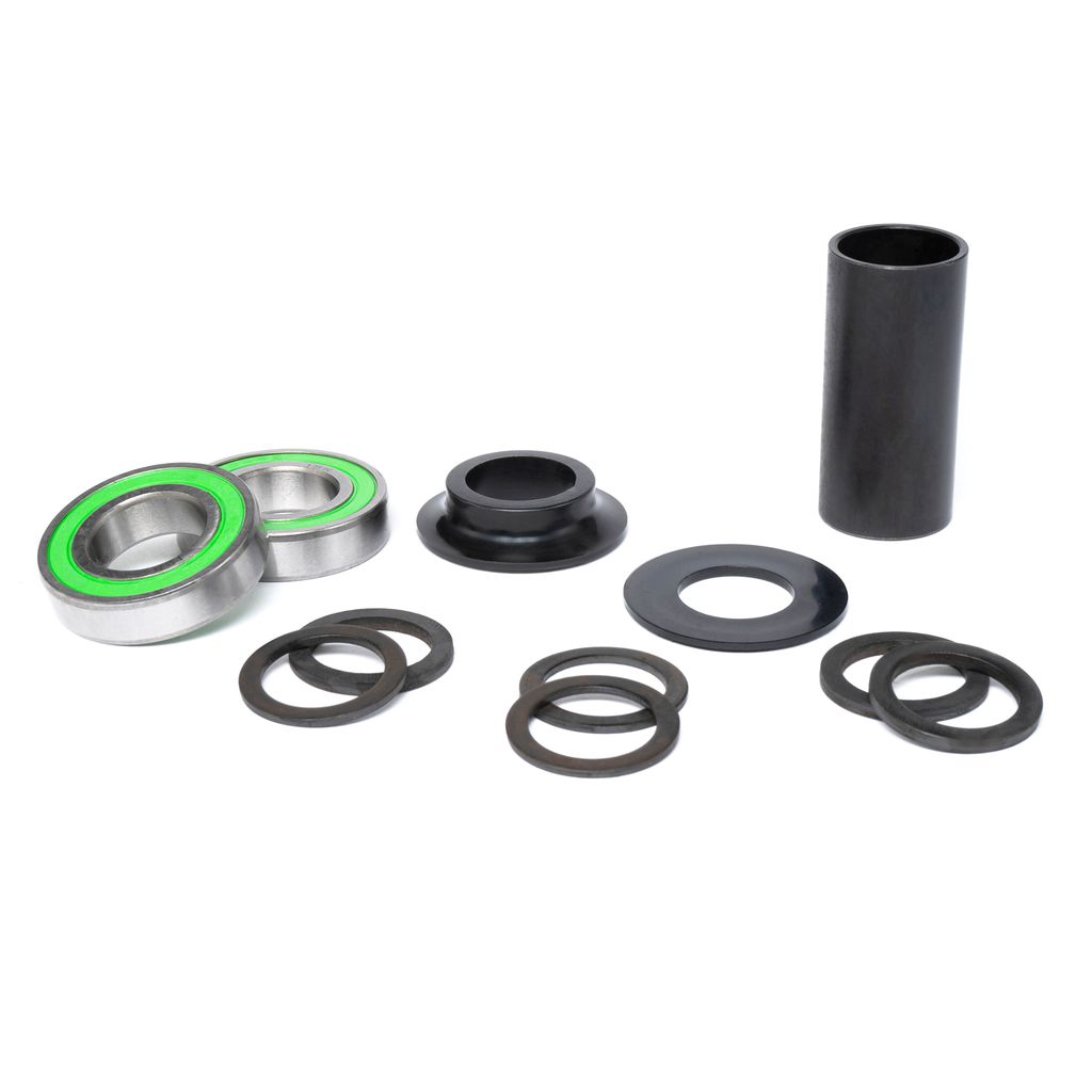 The Salt Rookie Spanish Bottom Bracket Set, featuring two green-sealed bearings, a black cylindrical tube, and various washers, is arranged on a white background.