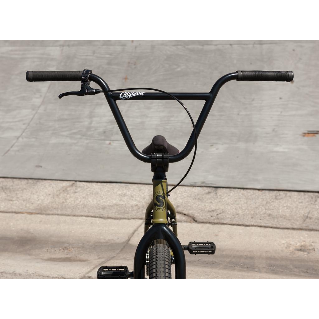 Close-up of the Sunday Wave Length 20 Inch BMX handlebar and front wheel on pavement. The straight handlebars, with visible brake cables, feature Odyssey parts in Gary Young's style.