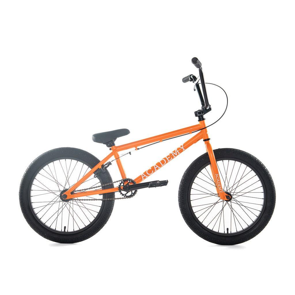 The Academy Trooper 20 Inch Bike is a vibrant orange BMX with a Hi-Ten steel frame, complemented by black handlebars, seat, and wheels. It boasts a robust design with sealed hubs for enhanced smoothness while riding.