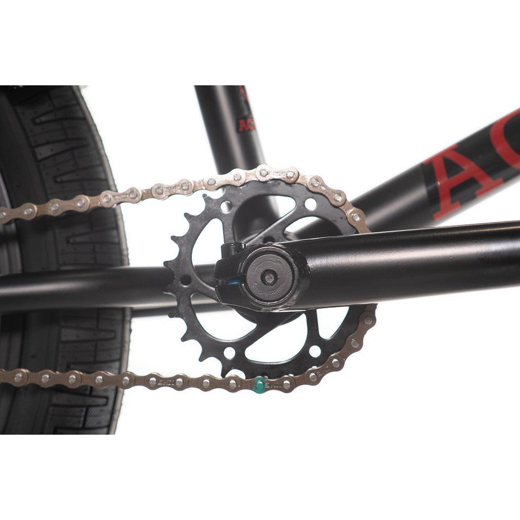 Close-up view of an Academy Desire 20 Inch Bike's black bicycle crankset with a chainring and chain connected to the rear wheel. The full Chromoly frame boasts a sleek design with black color and red lettering, complemented by a 21 inch top tube for optimal performance.