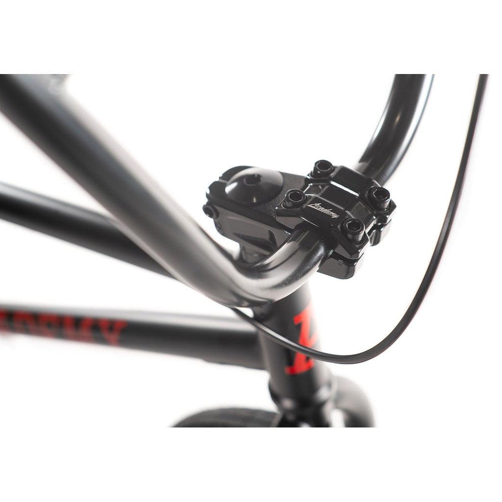 Close-up of a bicycle handlebar and stem connection on an Academy Desire 20 Inch Bike, featuring a black and grey color scheme, with a visible brake cable and a 21-inch top tube.