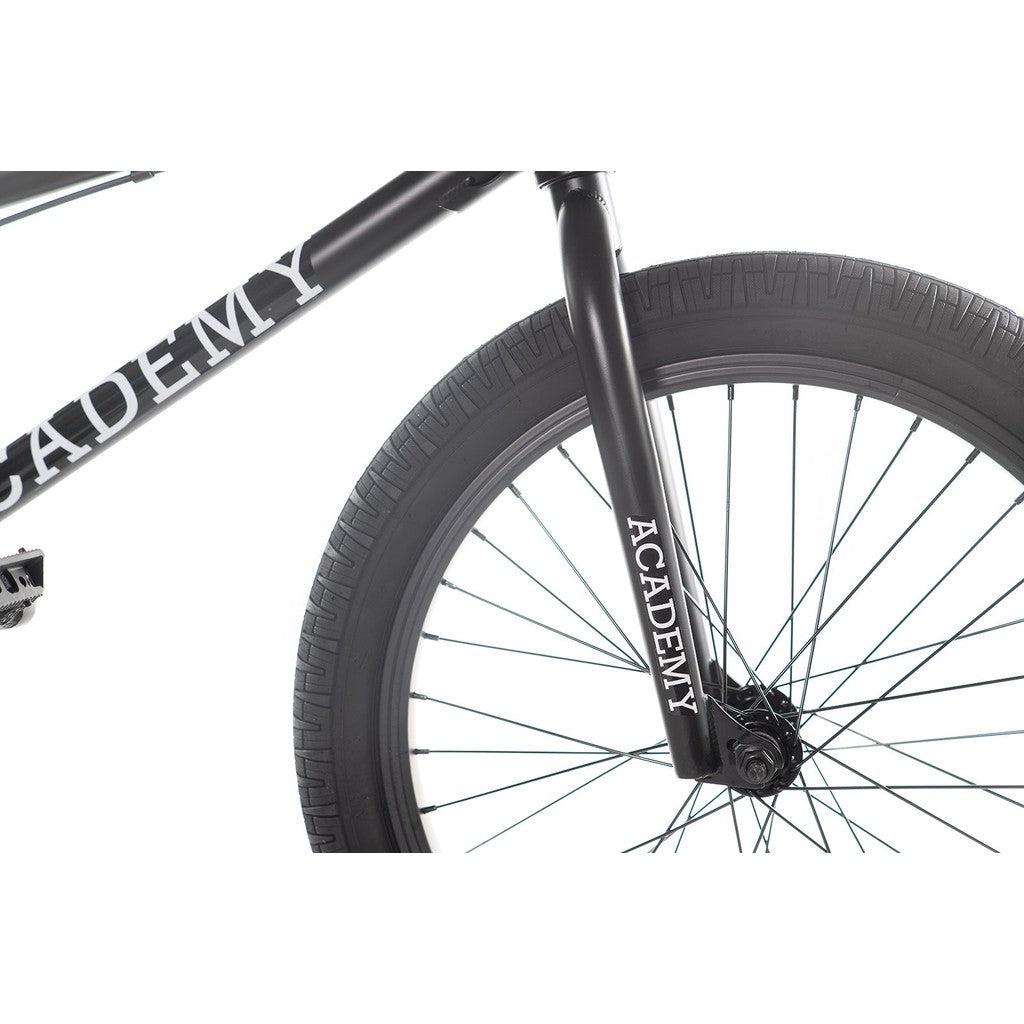 Close-up of a black wheel and fork from the Academy Aspire 20 Inch Bike, featuring the word "ACADEMY" printed in white on the fork, highlights a freestyle BMX bike with smooth sealed hubs for seamless performance.