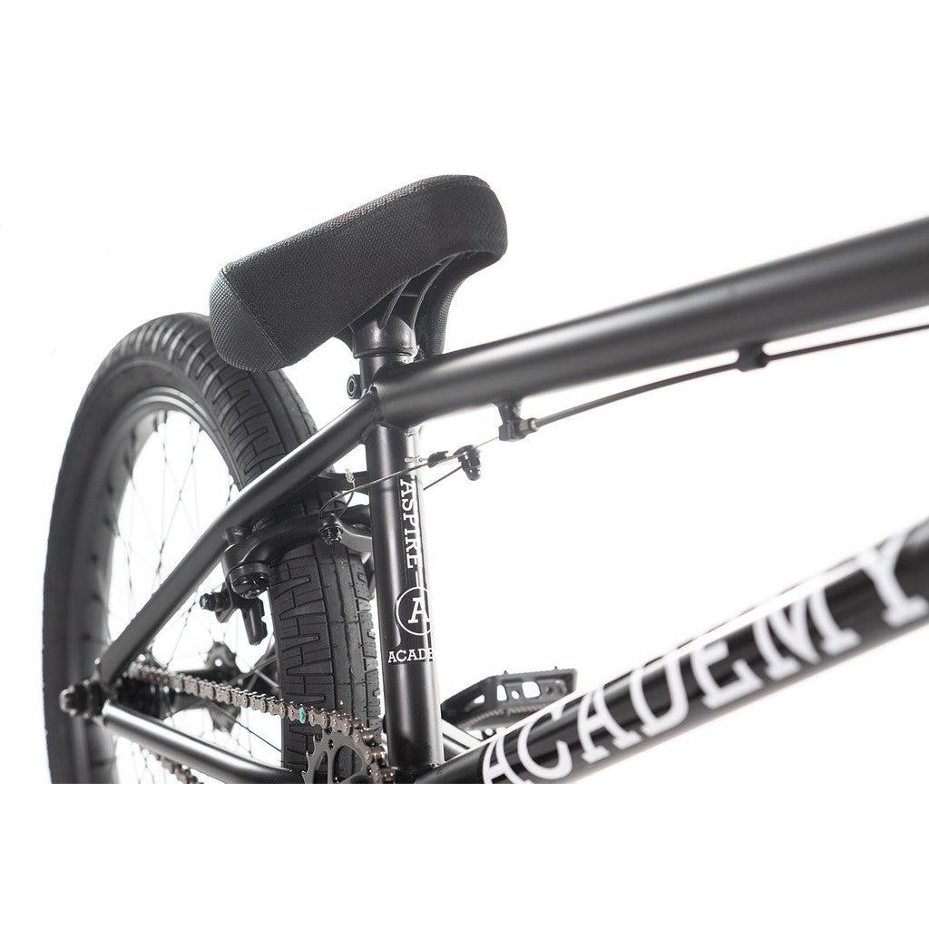 Close-up of the Academy Aspire 20 Inch Bike, featuring a freestyle BMX design with a black frame. The image highlights the seat, chain, and rear wheel, with "Academy" clearly displayed on the frame and complemented by sturdy CrMo bars.