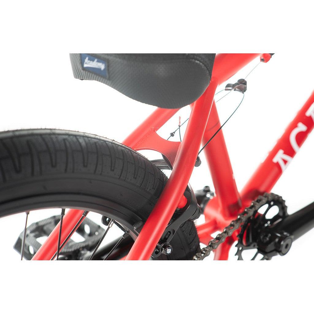 A close-up of the Academy Aspire 20 Inch Bike's red freestyle BMX frame highlights the rear wheel, tire, and seat. The brake and chain are visible, complemented by sealed hubs.