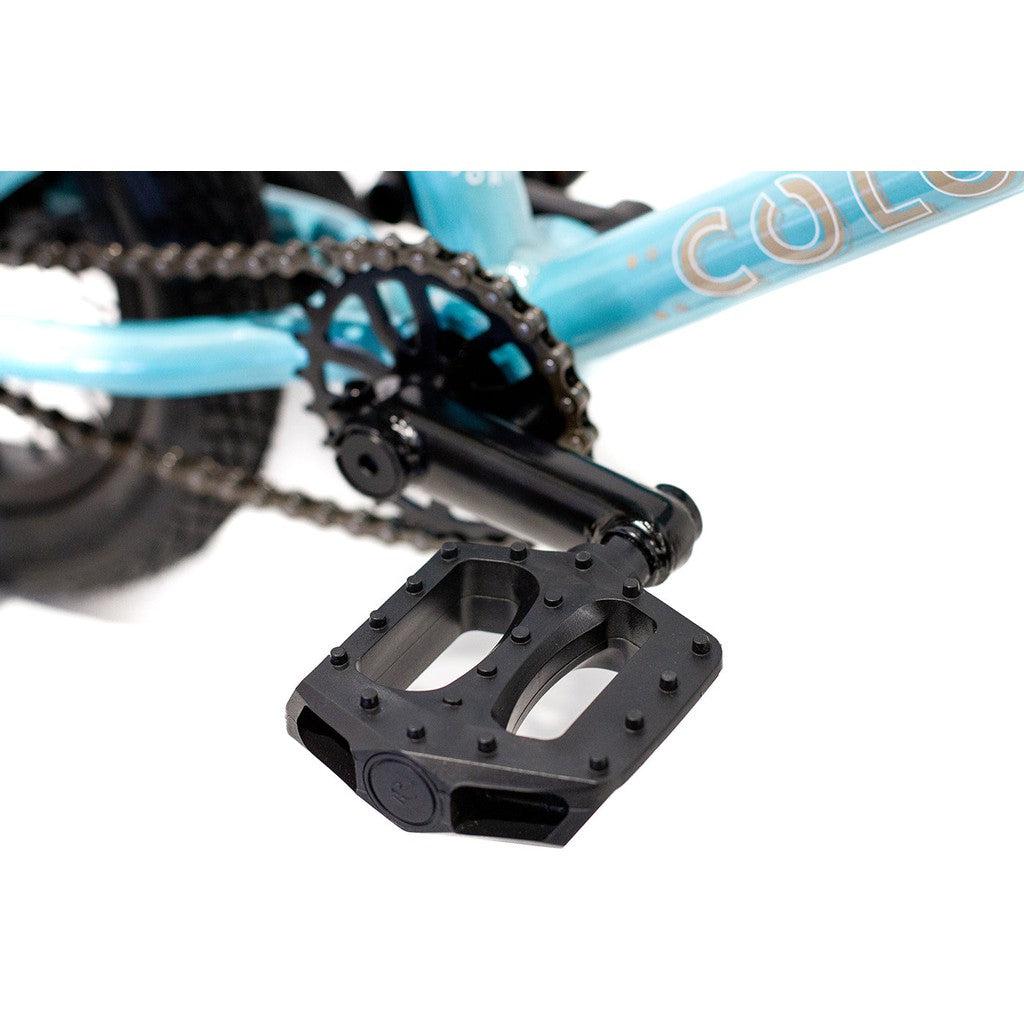 Close-up of the Colony Horizon 12 Inch Bike's pedal and chain mechanism on a blue, lightweight alloy frame. The black platform pedal, along with the crank arm and chainring, are clearly visible.