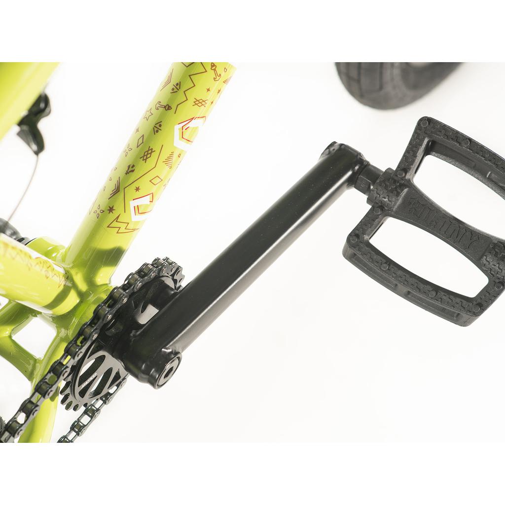 Close-up of a Colony Rico Pro 20 Inch Bike frame in green, showcasing yellow and orange geometric patterns. The black pedal and crank arm are distinct, with the bicycle chain partially visible. Limited edition BMX design.