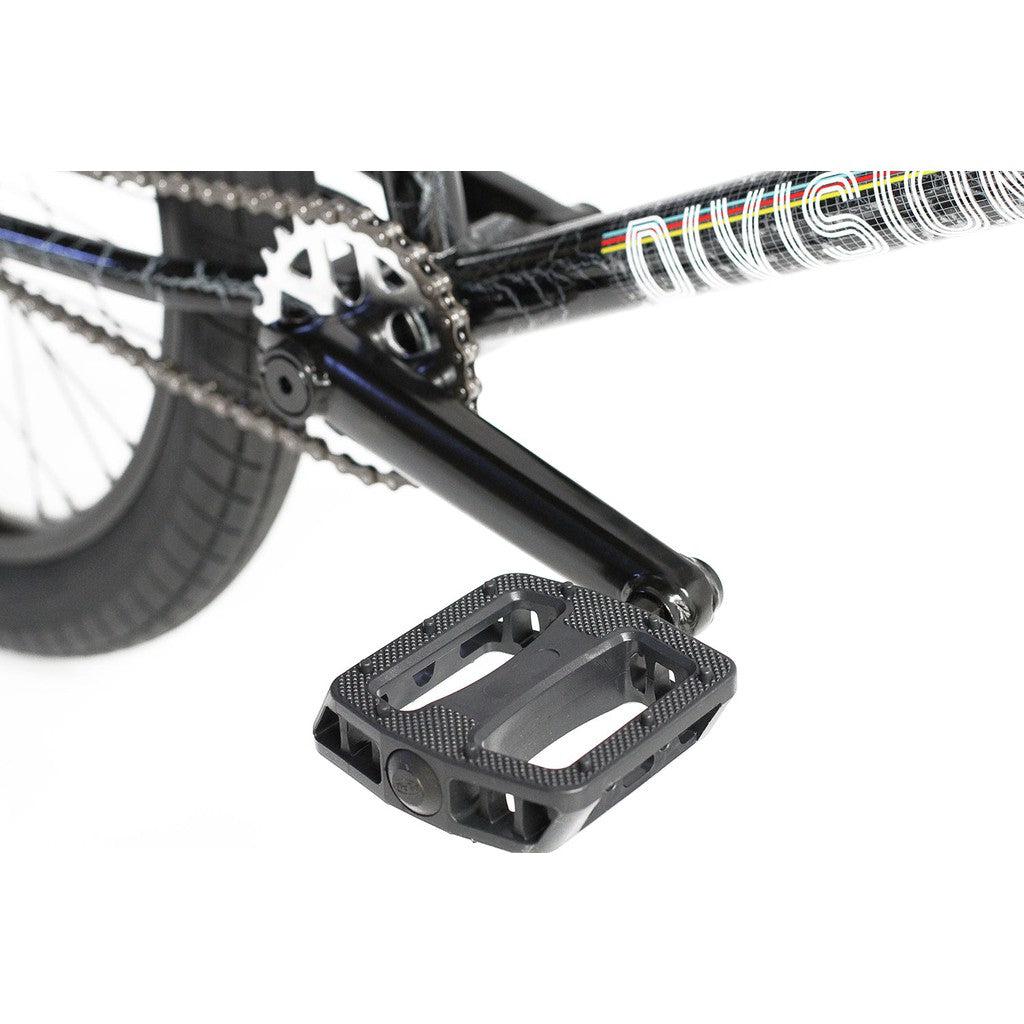 Close-up of the Division Fortiz 20 Inch Bike pedal and crank arm attached to its Chromoly frame. The tire, part of the chain, and chainring are also visible.