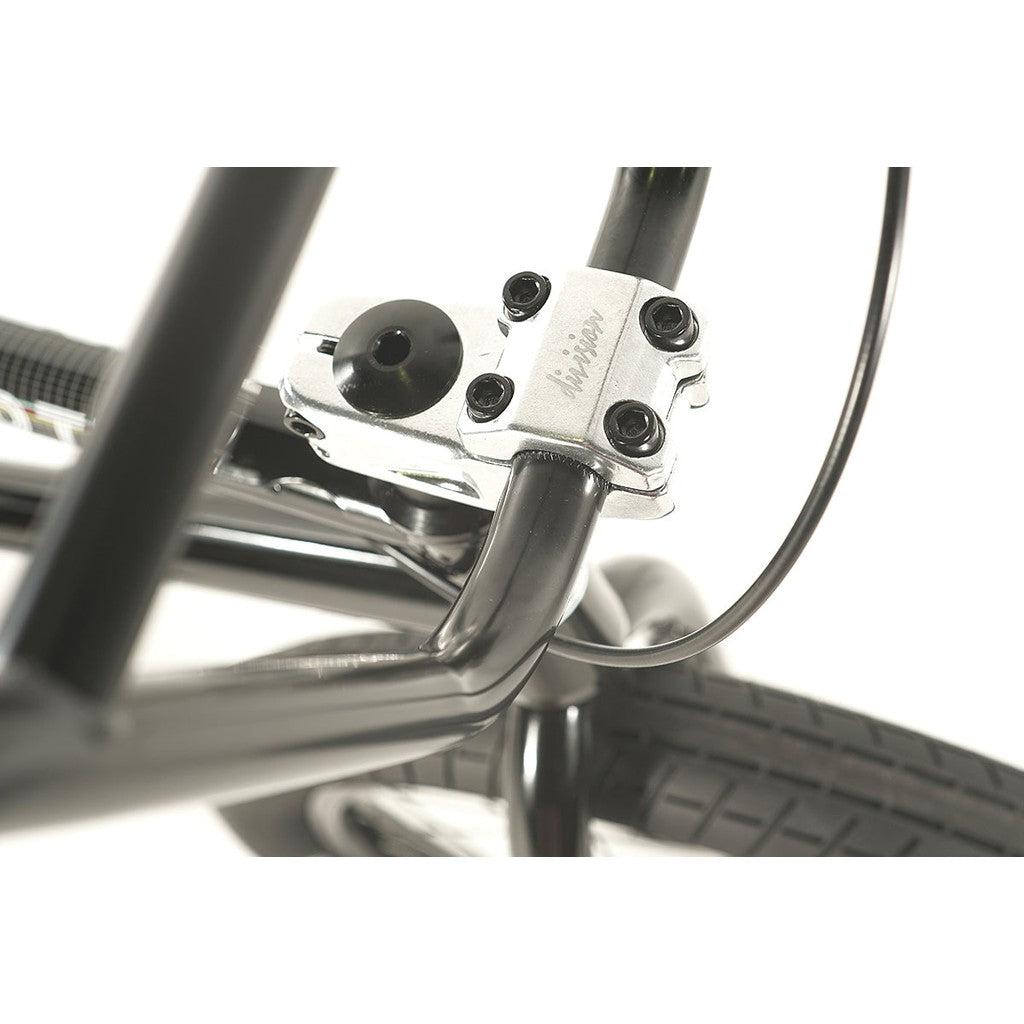 Close-up of the handlebar stem on a Division Fortiz 20 Inch Bike, showcasing a silver clamp that connects the handlebars to the front wheel assembly, with particular emphasis on the bolts and a portion of the tire.