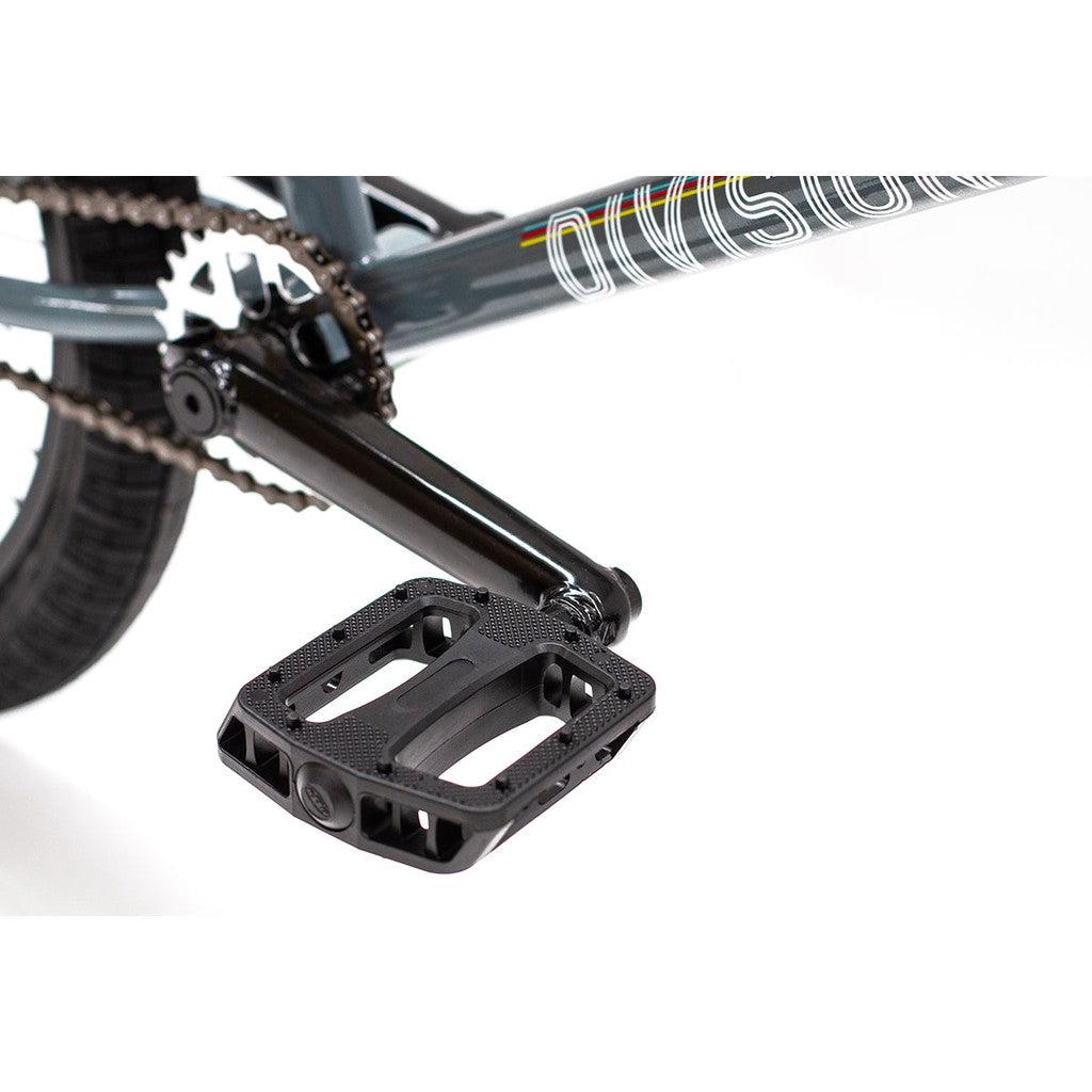 Close-up of the pedal and crank arm on a Division Fortiz 20 Inch Bike with the Chromoly frame partially visible. The black pedal features a textured surface for enhanced grip.