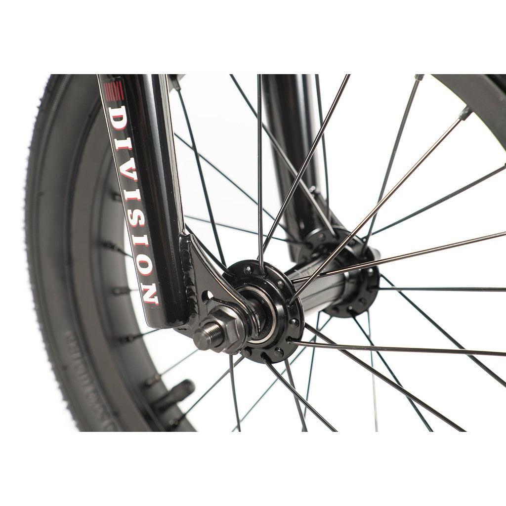 Close-up of a black bicycle wheel with spokes and a Division Blitzer logo on the fork, highlighting the sleek design of the Division Blitzer 14 Inch Bike, an entry-level freestyle BMX.