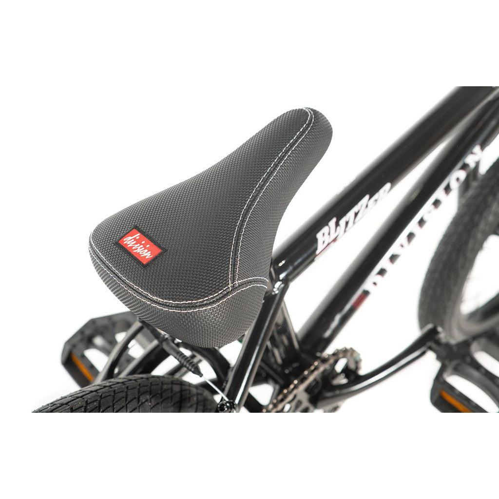 Close-up of a black bicycle seat featuring white stitching and a red logo on the Division Blitzer 14 Inch Bike frame, ideal for an entry-level freestyle BMX bike.