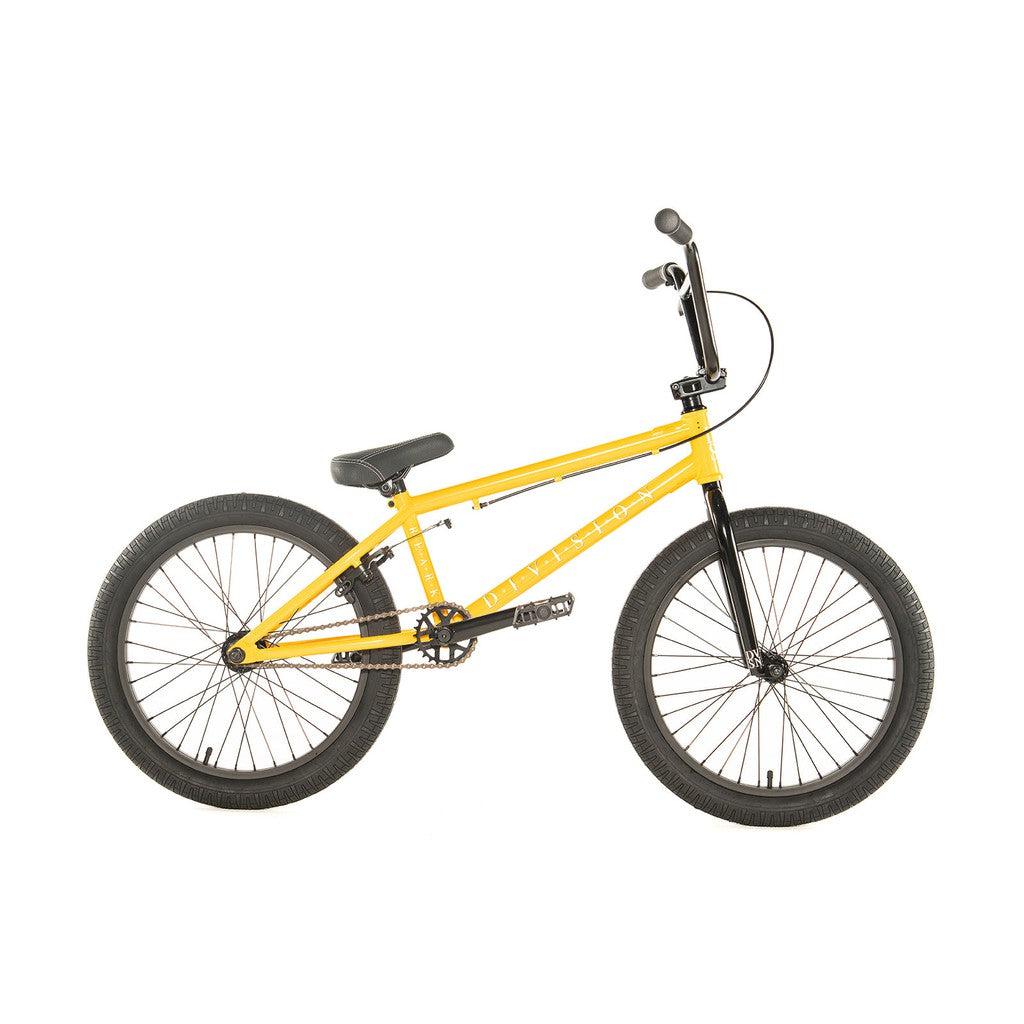 The Division Reark 20 Inch Bike is a yellow BMX featuring black handlebars, seat, and tires, displayed from the side on a white background. Built with Hi-Tensile steel for enhanced durability, it includes 3-piece cranks to ensure a smooth ride.