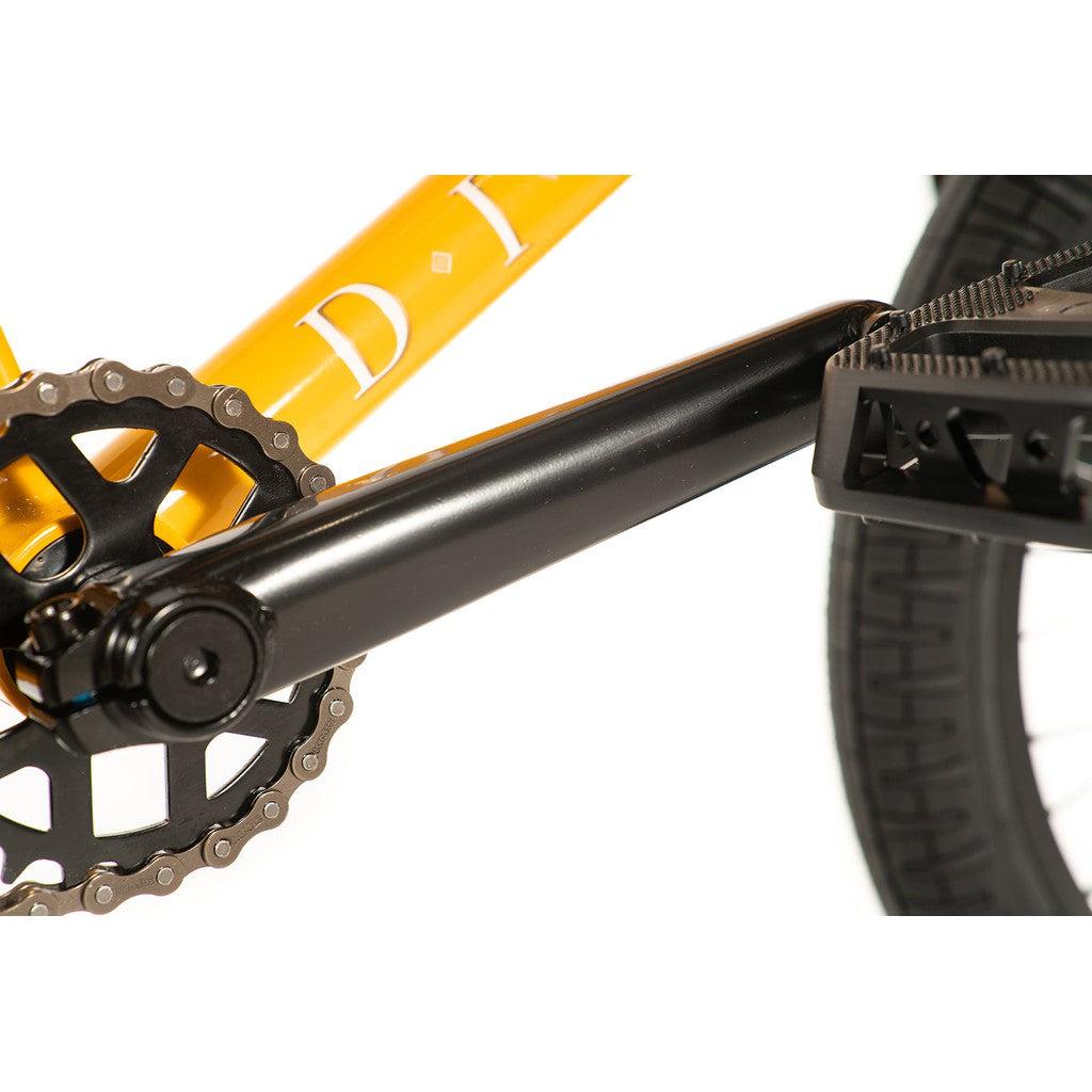 Close-up of the Division Reark 20 Inch Bike's drivetrain highlighting a black crank arm, chainring, and pedal set against its vibrant yellow frame, featuring robust Hi-Tensile steel components.