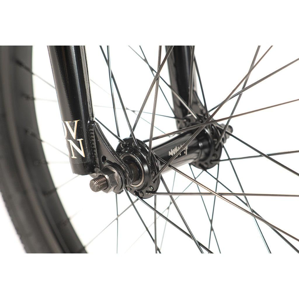 Close-up of a Division Reark 20 Inch Bike front wheel hub, featuring spokes extending from the hub to the rim, and a black fork marked with white initials. The bike boasts a durable frame constructed from Hi-Tensile steel for enhanced strength.