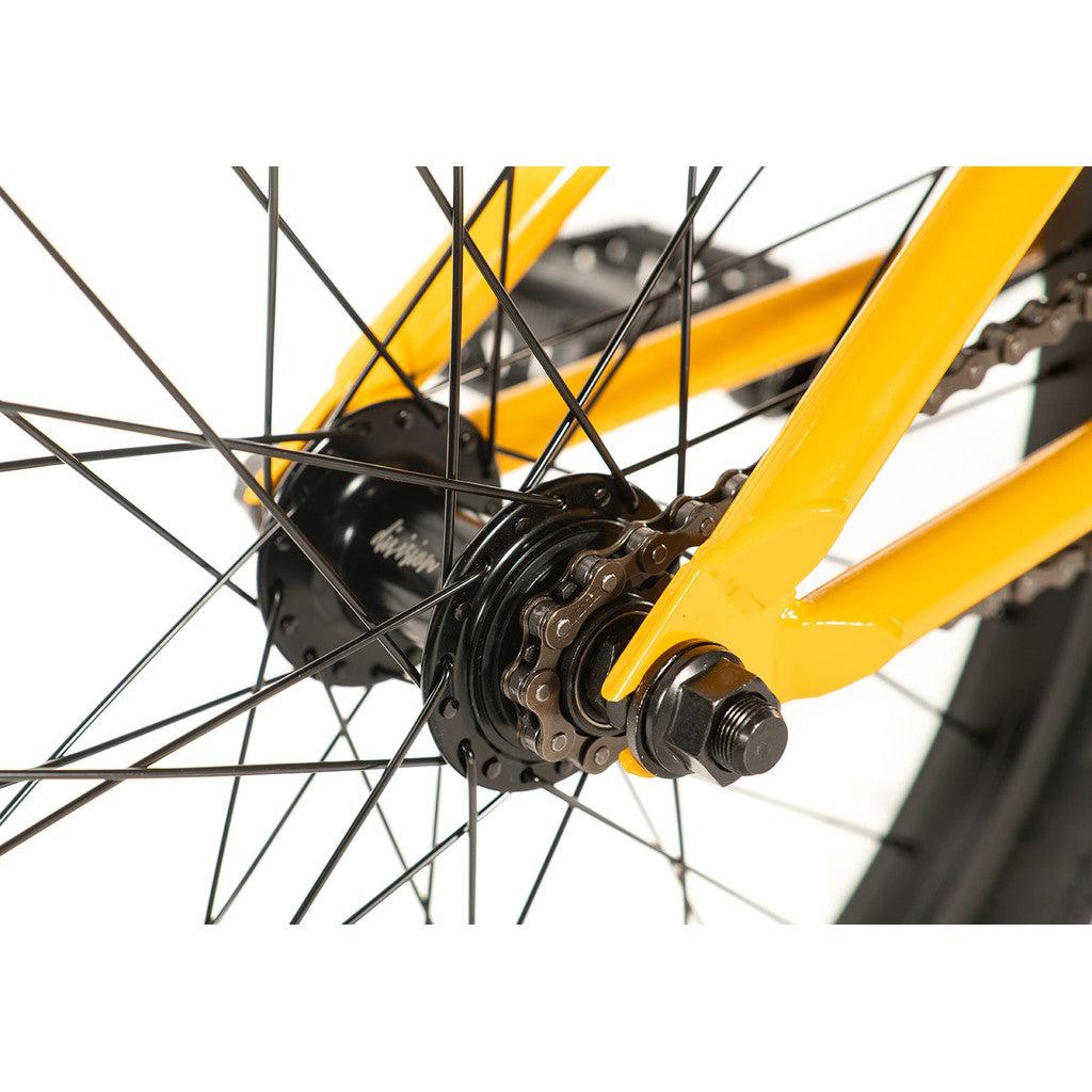 Close-up of a Division Reark 20 Inch Bike's yellow frame, showcasing the rear wheel with its spokes, hub, and chain mechanism. The bike features durable 3-piece cranks against a plain background.