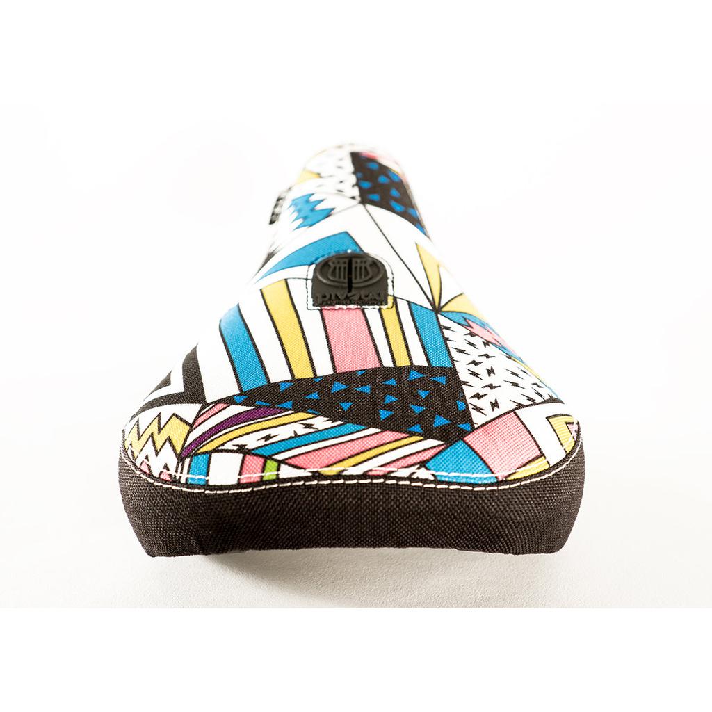 The Colony X Fist Pivotal Seat features extra grippy fabric with a vibrant geometric pattern of triangles, zigzags, and shapes in pink, blue, yellow, and black.